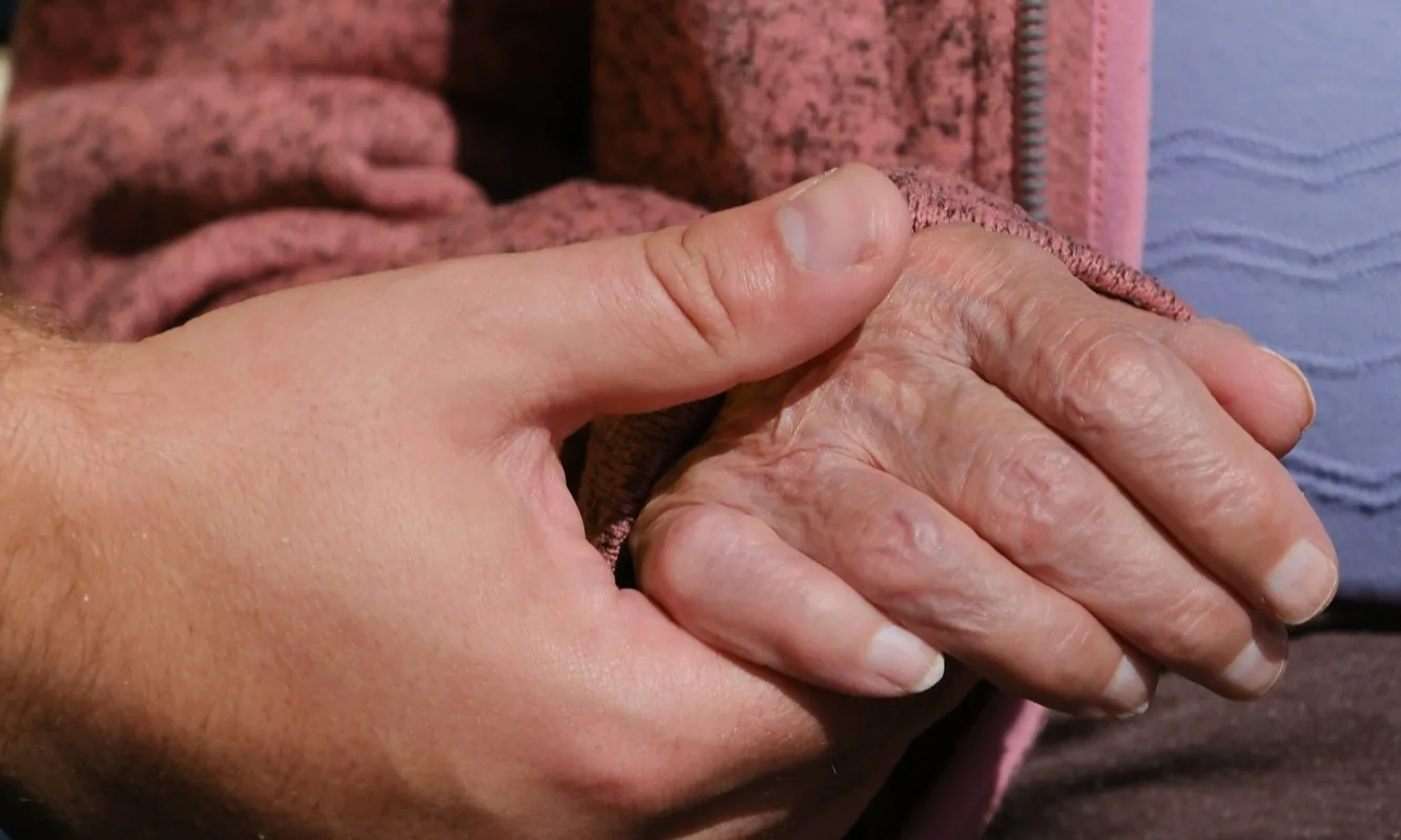 A younger hand gently holding an older person's hand
