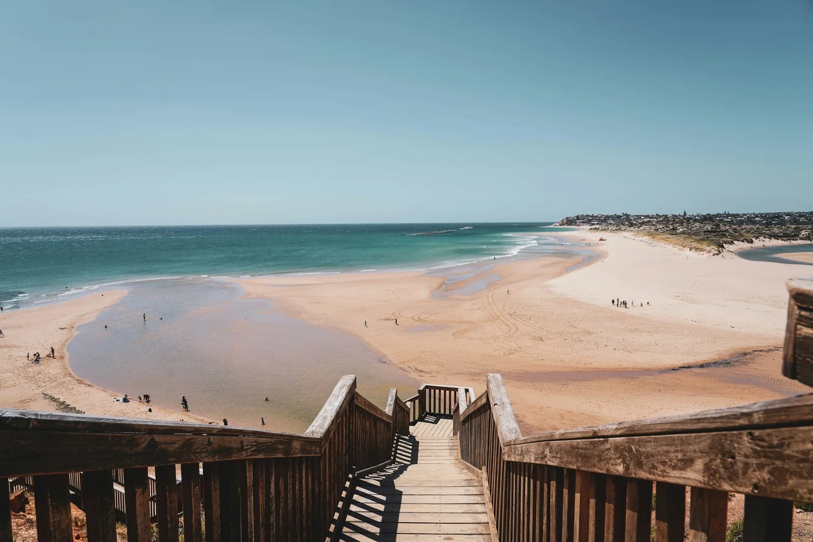 Timber stairs leading down to a wide sandy beach on a sunny day