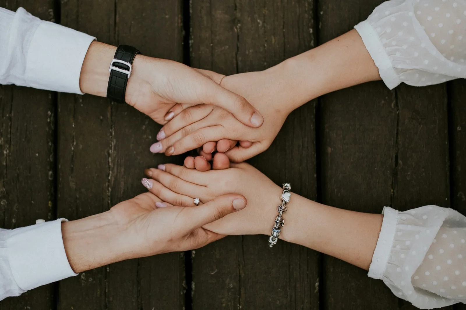 Four people resting their hands together on a wooden table