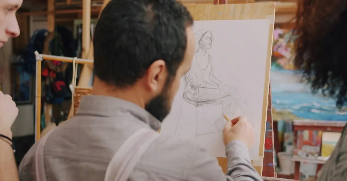 A man sketching a portrait at an easel in an art studio