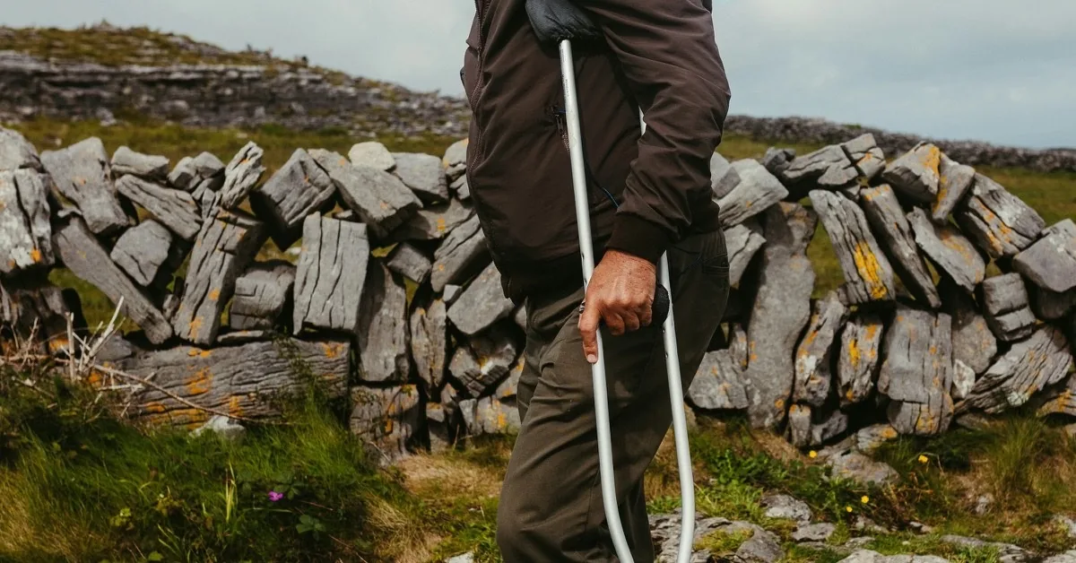 A person using a white cane walks beside a dry stone wall