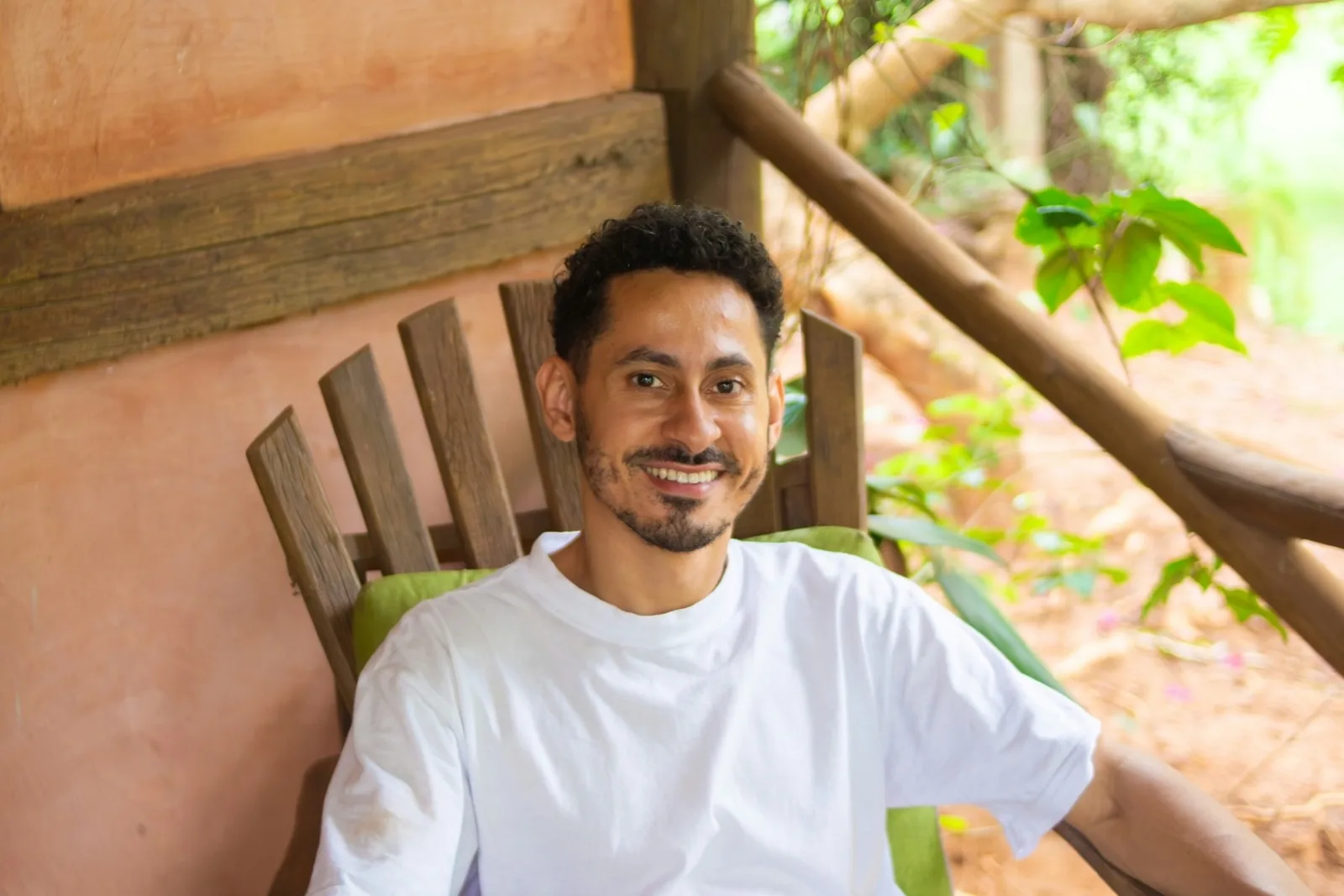 A smiling man sitting in a wooden chair on a veranda
