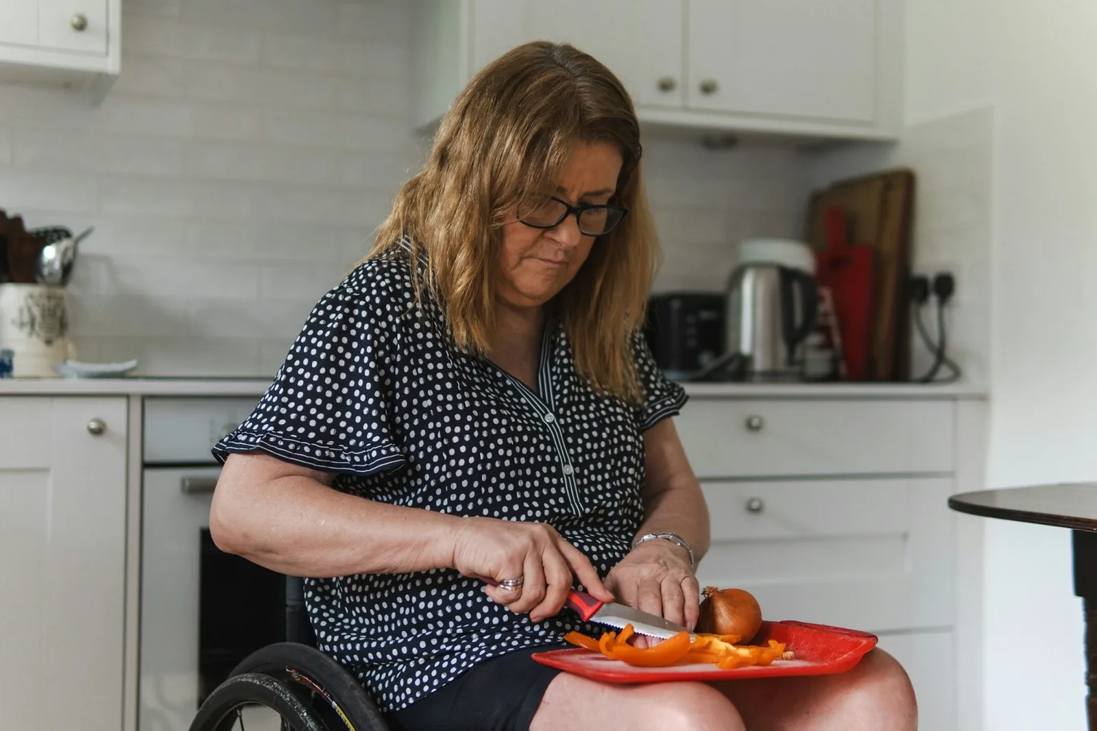 A woman using a wheelchair prepares vegetables in her kitchen
